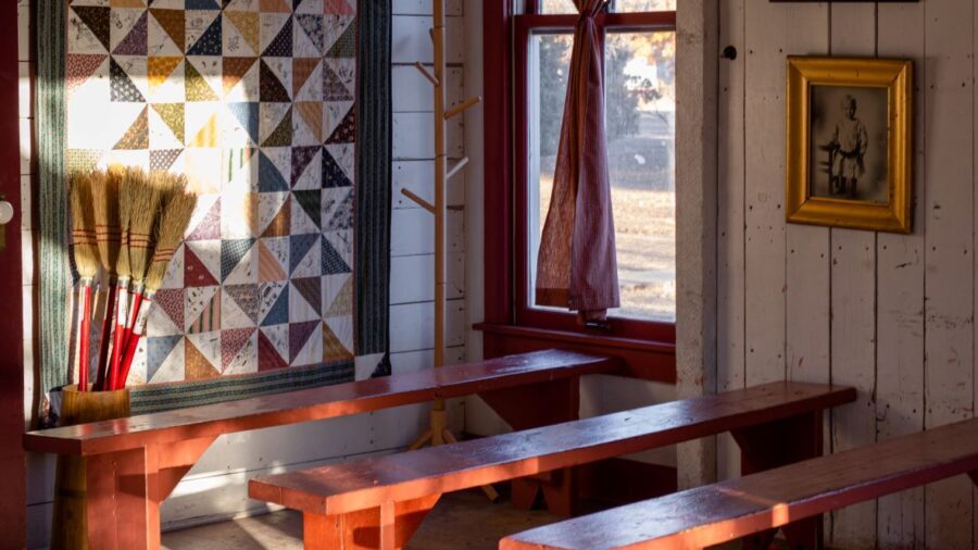 Sunlit room with wooden benches, a quilt on the wall, vintage photo, and window curtains