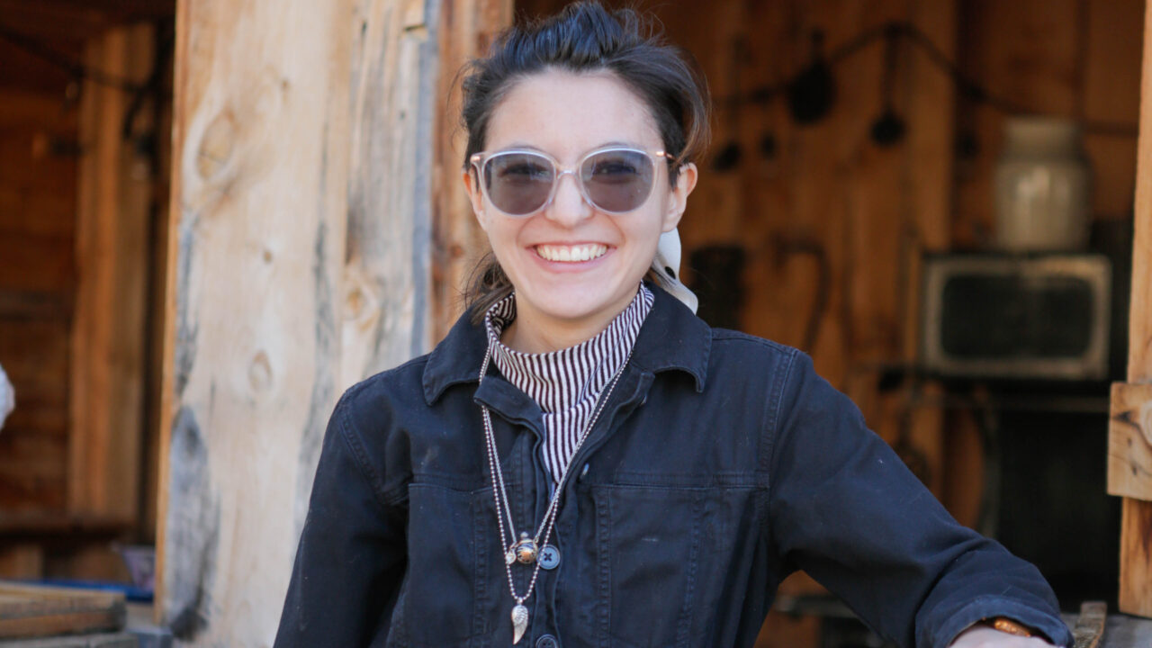 Persona sonriendo al aire libre, con gafas de sol y una chaqueta negra