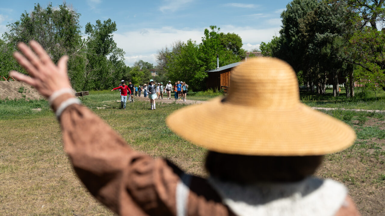 Person in a straw hat waves at approaching group of people outdoors