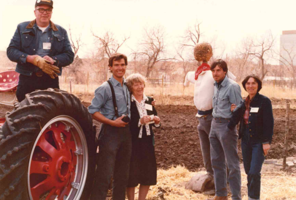 Un grupo de personas de pie junto a un tractor y un espantapájaros en un entorno rural