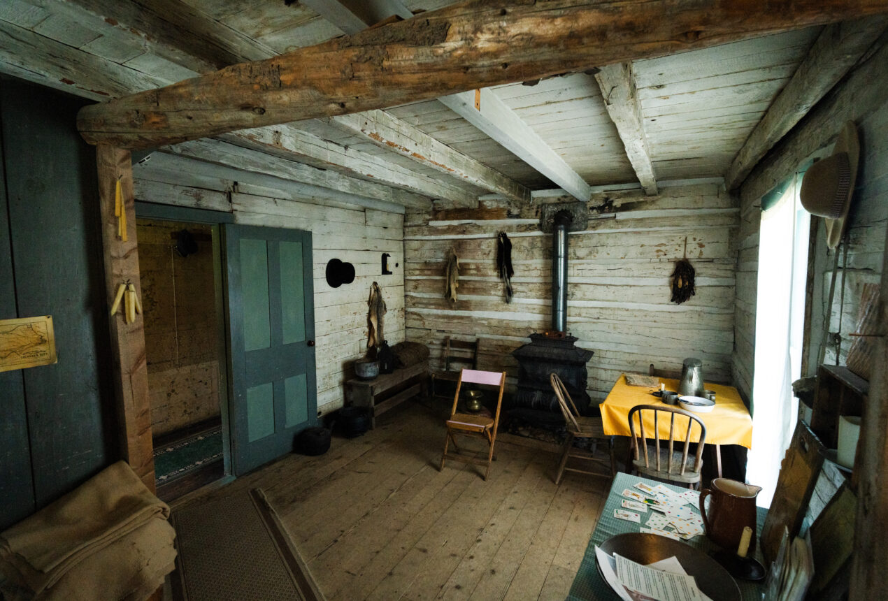 Interior de una cabaña rústica de madera con estufa, sillas y mesa
