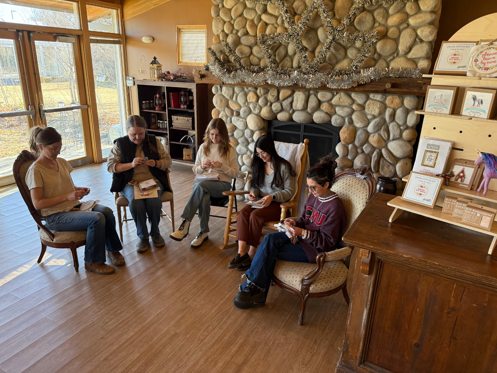 Five people sitting in a cozy room, engaged in embroidery activities