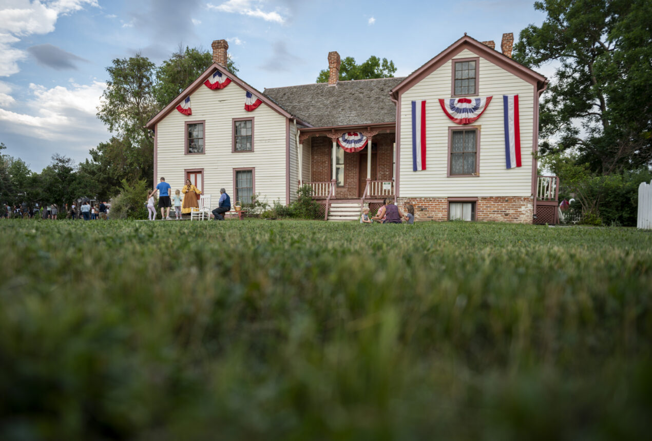 Casa histórica decorada con banderines rojos, blancos y azules; gente reunida en el porche y en el jardín