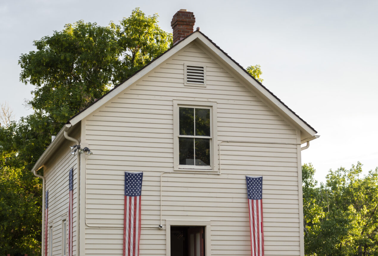 Casa blanca con banderas estadounidenses, rodeada de árboles verdes