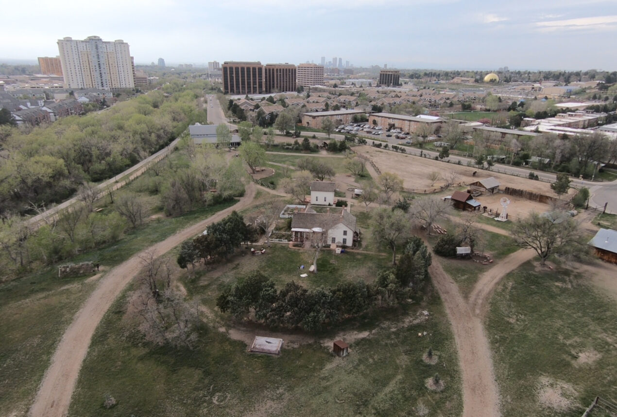 Vista aérea de una zona rural con casas, árboles y caminos de tierra, con edificios urbanos al fondo