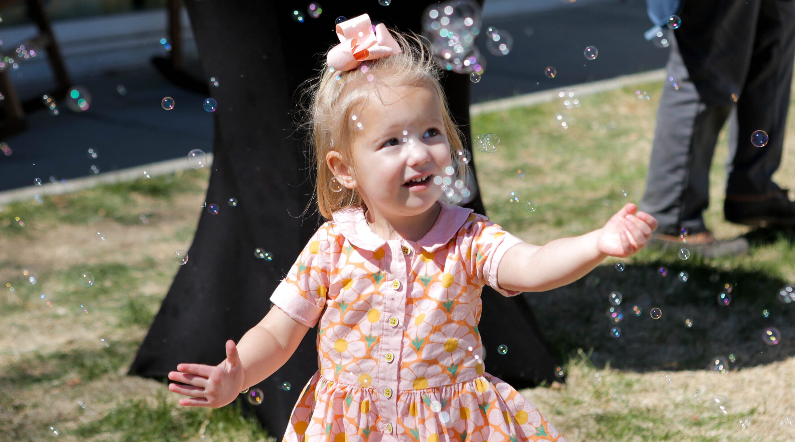 Young child in a pink dress joyfully playing with bubbles outdoors