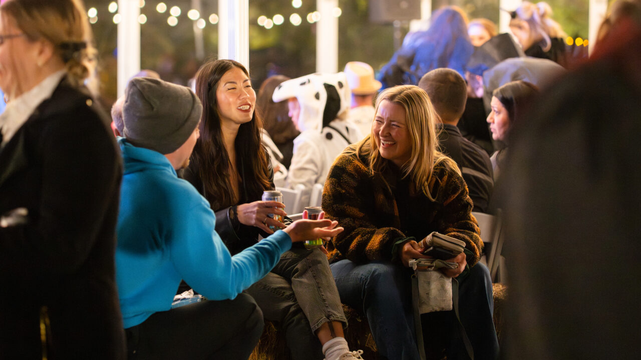 People chatting and laughing at an outdoor event with festive string lights