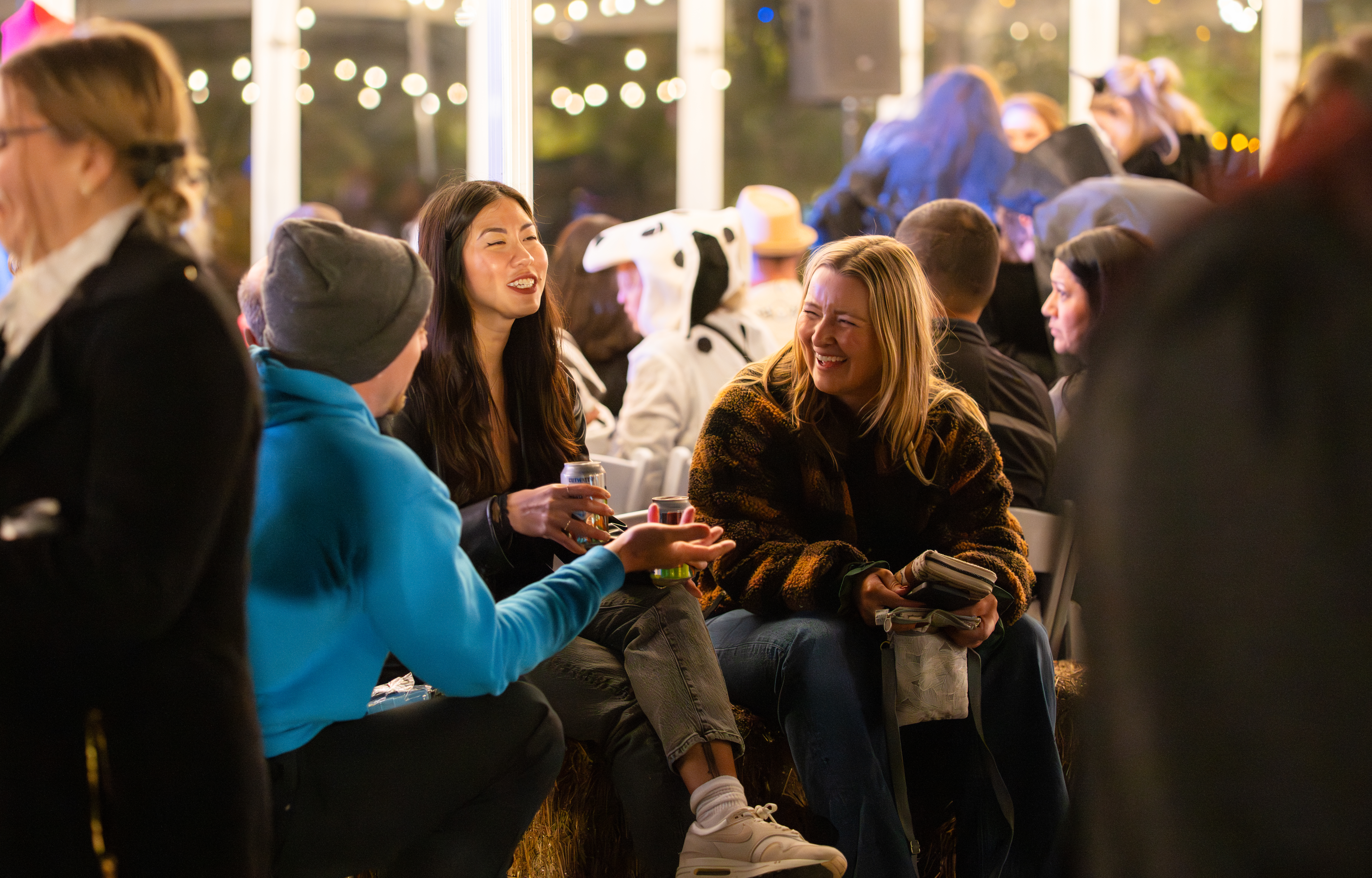 People chatting and laughing at an outdoor event with festive string lights