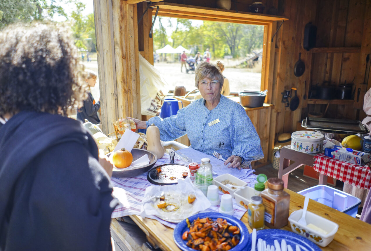 Una mujer mayor con un vestido azul sirviendo comida en un puesto rústico al aire libre