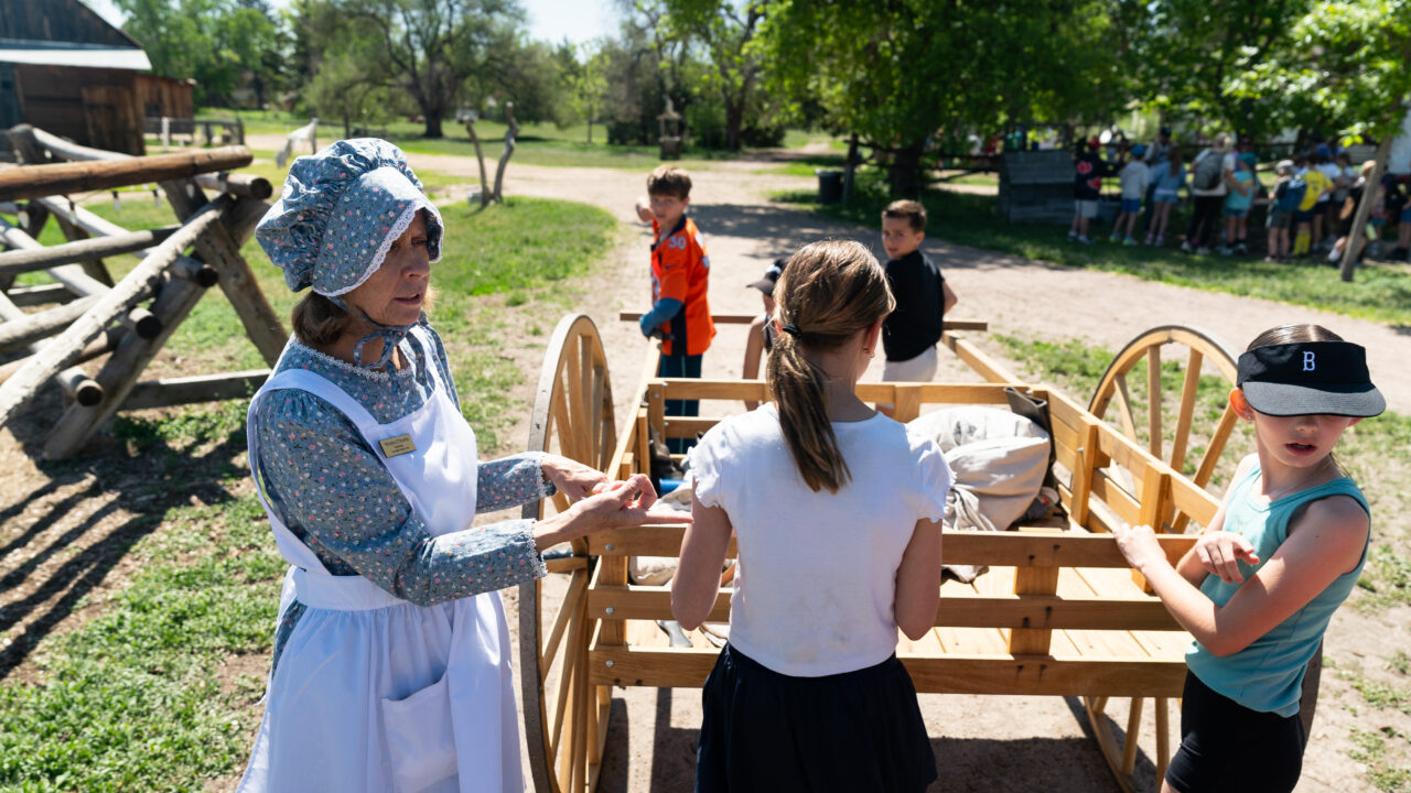 Woman in historical attire demonstrating to children at outdoor event