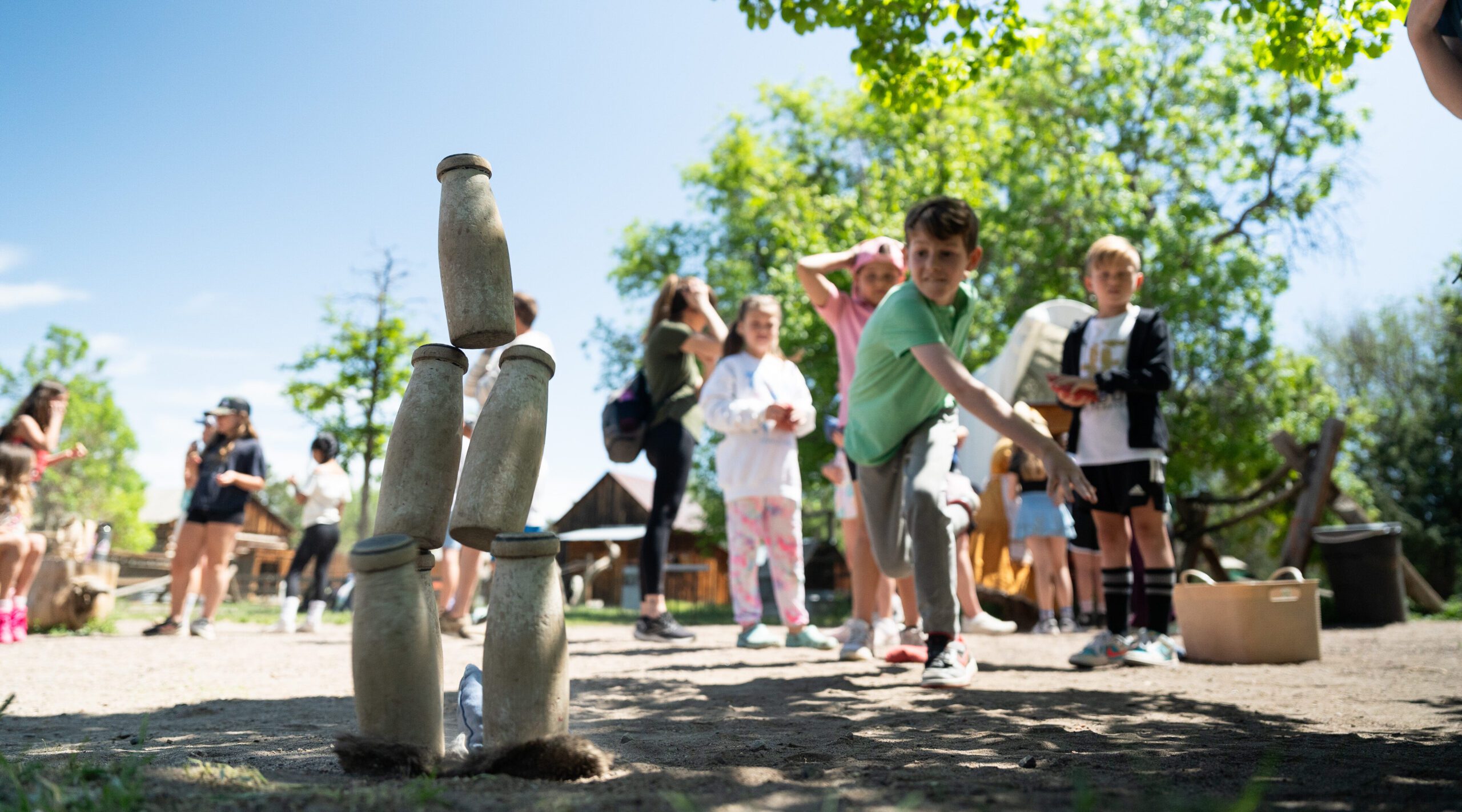 Children playing ring toss game outdoors, focus on stacked bottles