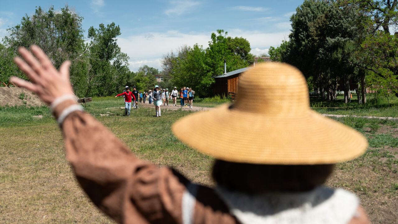 Person in straw hat waves at approaching group in park