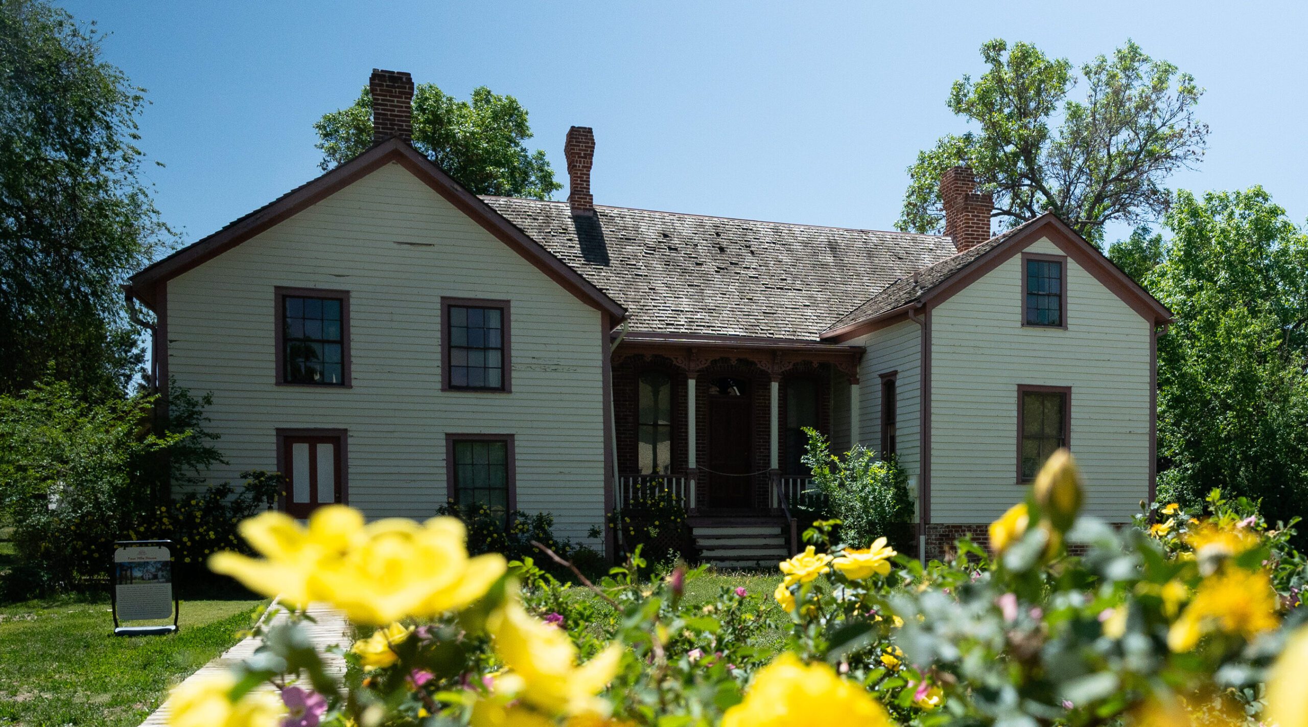 Casa histórica de madera con flores amarillas en primer plano, rodeada de árboles