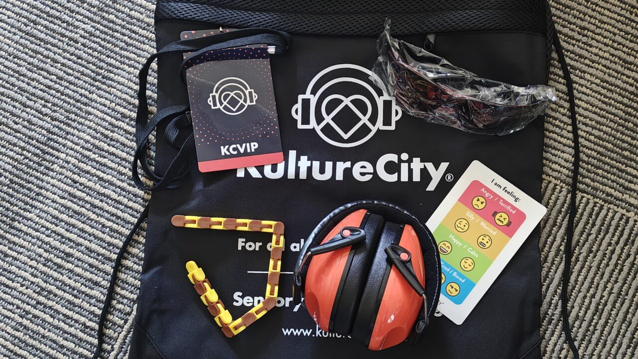 Bolsa sensorial de KultureCity con auriculares, gafas de sol, tarjeta de emociones y una insignia con la inscripción «KCVIP»